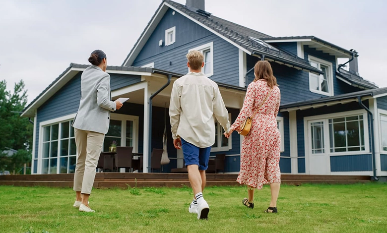 Three people walking towards a modern blue house on a grassy lawn.