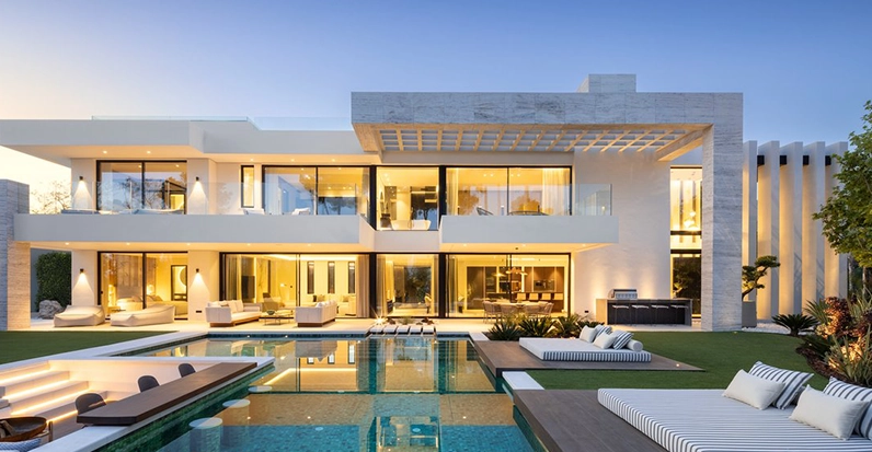 Modern luxury home with large pool and outdoor seating area at dusk.