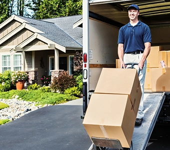 Mover unloading boxes from a truck in front of a suburban house.